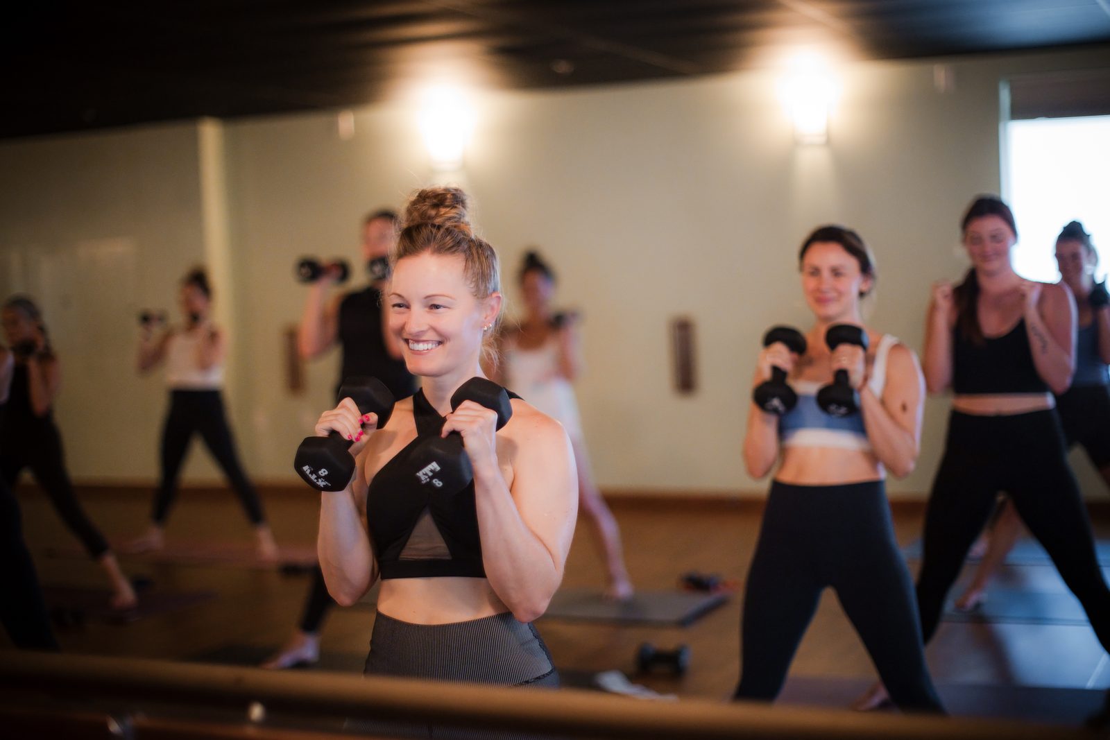 Students smiling as they lift hand weights in a sculpt class