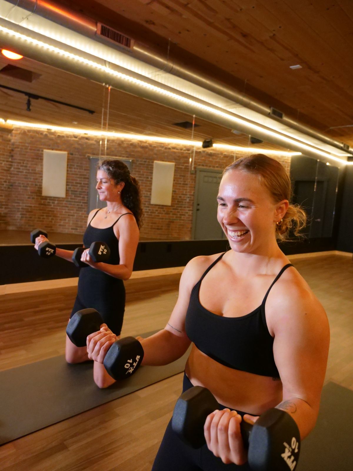 Alex Gaon smiling as she lifts hand weights in a bootcamp class